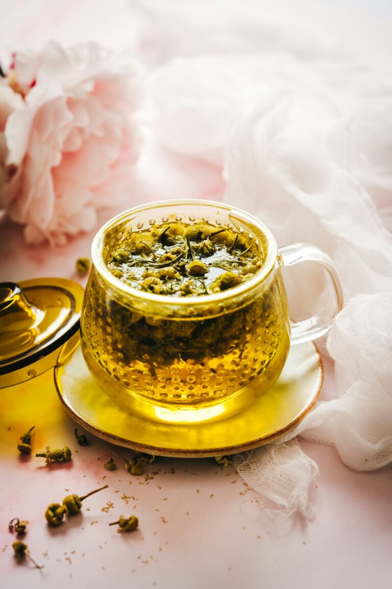 Steaming cups of ginger, chamomile, and peppermint tea beside fresh herbs on a kitchen table.